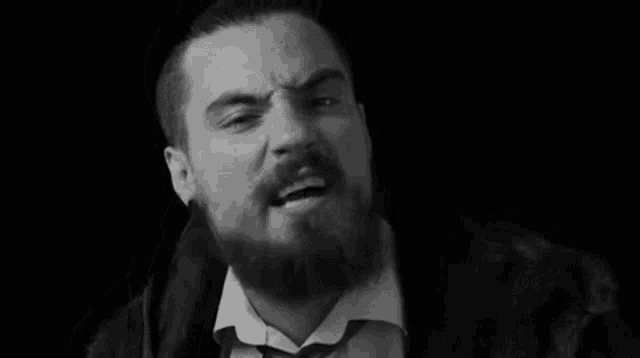 a man with a beard wearing a fur coat and tie is making a funny face in a black and white photo .