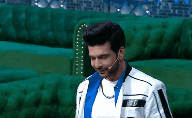 a man wearing a white jacket and a blue shirt stands in front of a green couch