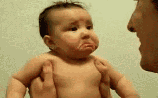 a baby is being held by a man and making a funny face .
