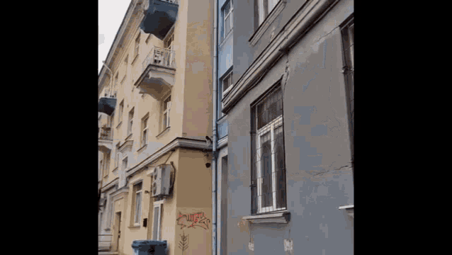 a building with graffiti on the side of it and a blue trash can .