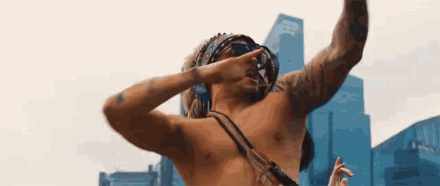 a shirtless man wearing a bandana and sunglasses is dancing in front of a city skyline