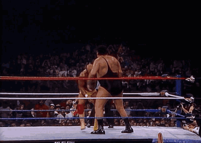 two men are wrestling in a ring with a crowd watching and a sign that says ' wwe ' on it