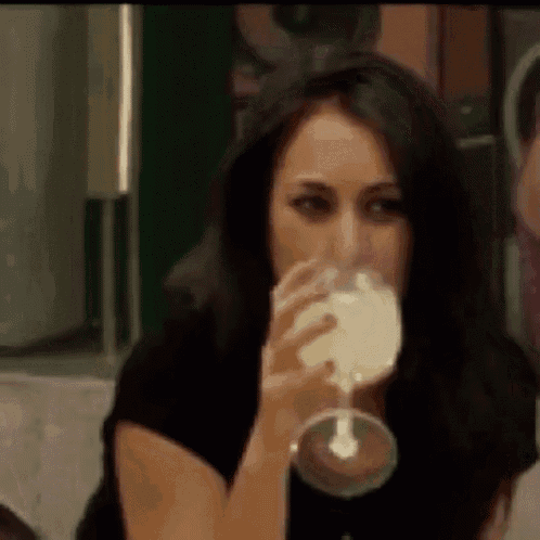 a woman is drinking a glass of wine while sitting at a table .