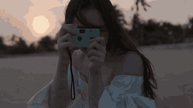 a woman taking a picture with a camera with the sun behind her