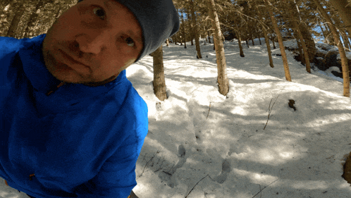 a man in a blue jacket stands in the snow looking at the camera