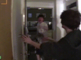 a man is opening a door in a room with a reflection of another man in the mirror .