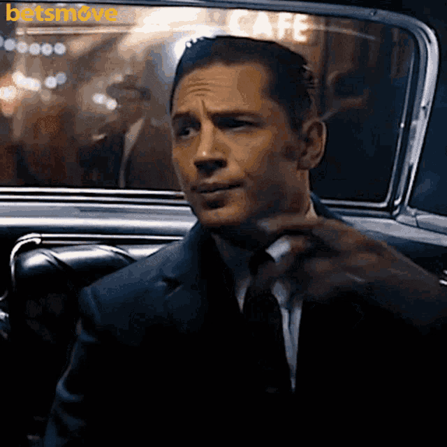 a man in a suit and tie is sitting in a car with a cafe sign in the window