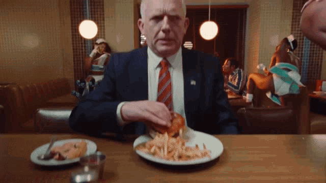 a man in a suit and tie is sitting at a table eating a hamburger