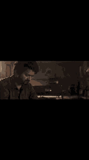 a man in a blue shirt is standing in a dark room holding a bottle .