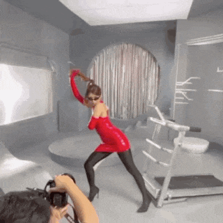 a woman in a red dress is dancing in a room while a man takes a picture .