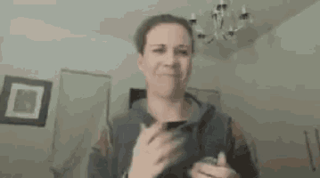 a woman is standing in a room holding a glass of wine and a cell phone .