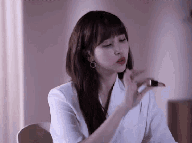 a woman wearing a white jacket is applying lipstick to her lips .