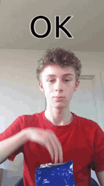 a young man in a red shirt is holding a bag of chips with the word ok written above him
