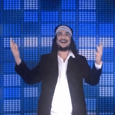 a man with long hair and a headband is standing in front of a blue background
