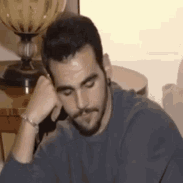 a man with a beard is sitting at a table with his head on his hand .