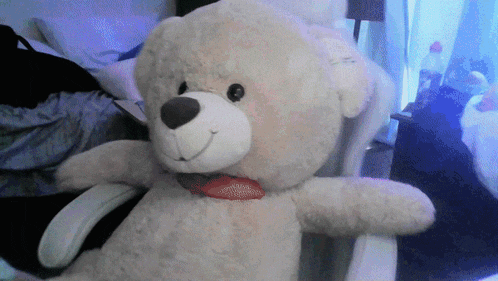 a teddy bear wearing a red bow tie is sitting in a chair