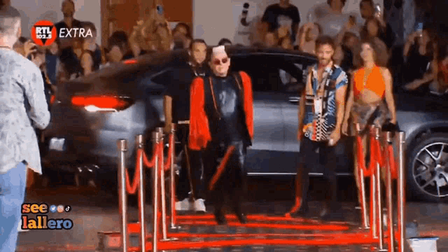 a group of people are walking down a red carpet in front of a car with ktl extra written on the bottom