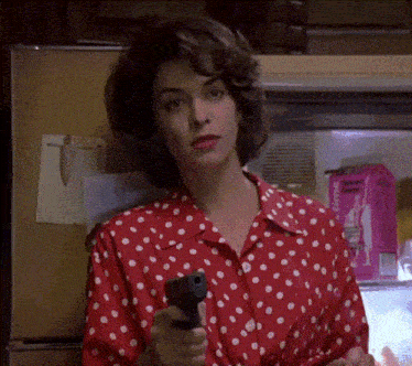 a woman in a red and white polka dot shirt is pointing a gun at the camera