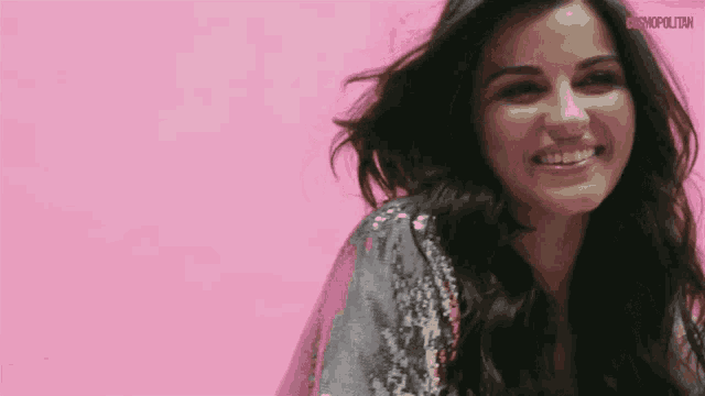 a woman is smiling in front of a pink wall with the word cosmopolitan on it