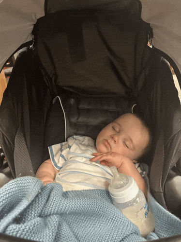 a baby is sleeping in a stroller while holding a bottle that says ' nuby ' on it