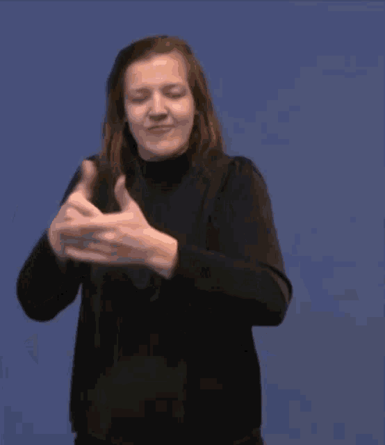 a woman in a black dress is making a gesture with her hands on a blue background .