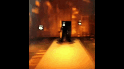 a blurry picture of a person standing in a dark room with a light shining on them .