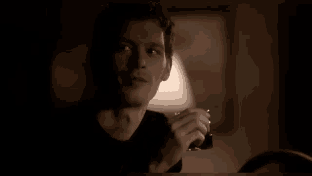 a man in a black shirt is sitting in a dark room holding a lighter .