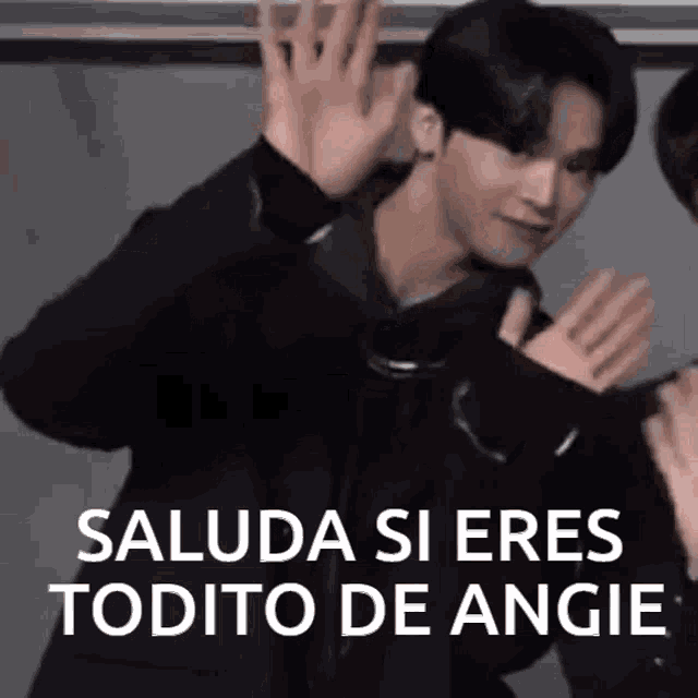 a man in a black jacket is waving his hands in front of a sign that says saluda si eres todito de angie