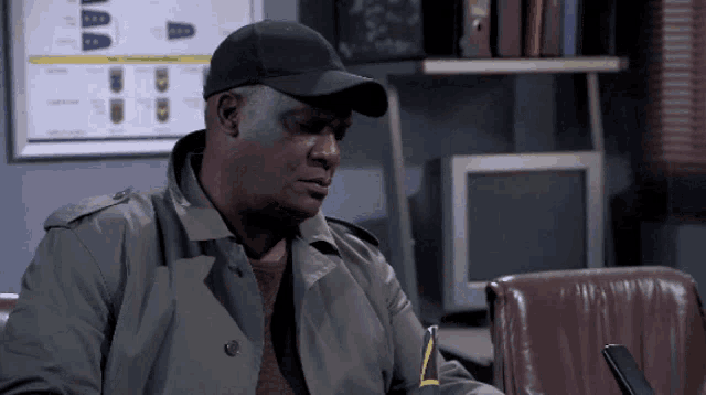 a man wearing a hat and a trench coat is sitting in front of a computer