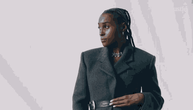 a woman is wearing a grey jacket and a necklace with the word bustle on the bottom