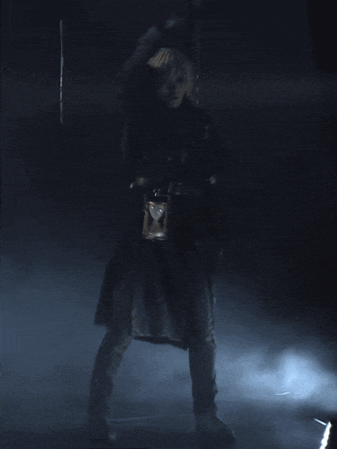 a person in a black coat holding a sword in a dark room
