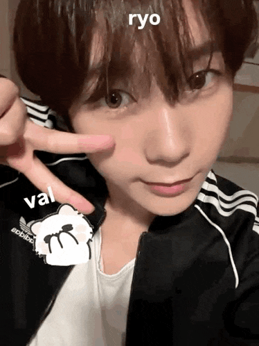 a young man is taking a selfie with his fingers on his face while wearing a black adidas jacket .