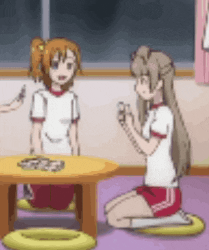 two anime girls are sitting at a table in a room talking to each other .