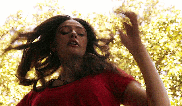 a woman in a red shirt is standing in front of a tree .