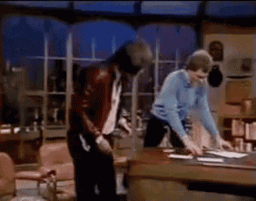 a man in a red leather jacket is standing next to a woman in a blue shirt at a desk