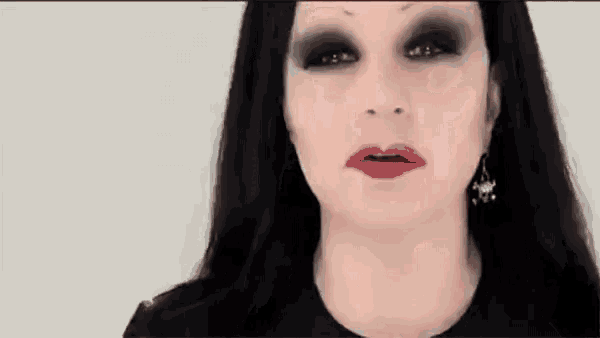 a woman with long black hair and red lipstick is wearing a black top and earrings .