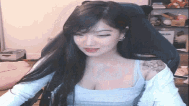 a woman is sitting in a gaming chair with her eyes closed and a tattoo on her shoulder .