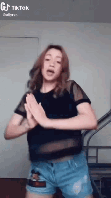 a woman in a black shirt and blue shorts is dancing on a tik tok video .