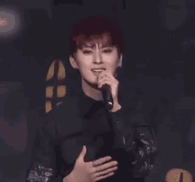 a young man is singing into a microphone on stage .