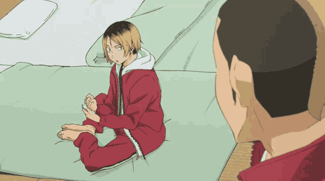 a man in a red jacket sits on a bed next to another man in a red jacket