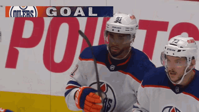 two hockey players are standing in front of a banner that says oilers goal