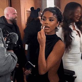 a woman in a black dress is applying lipstick to her lips while standing in a crowd .