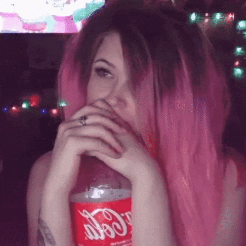 a woman with pink hair drinking a bottle of coca cola