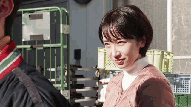 a woman in a pink jacket and white turtleneck stands next to a man in a black jacket