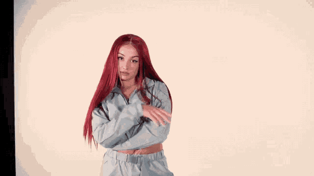 a woman with red hair is standing in front of a white wall with her arms crossed and smiling .
