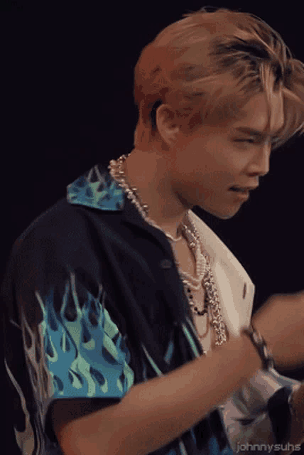 a close up of a man wearing a shirt with flames on it and a necklace
