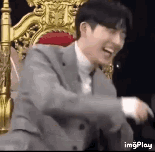 a man in a suit and tie is sitting on a throne laughing .