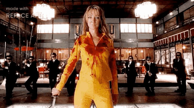 a woman in a yellow jumpsuit is holding a bloody knife .