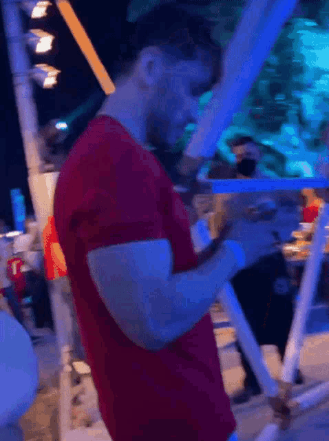 a man in a red t-shirt is looking at his phone