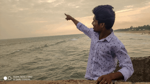 a redmi note 7 pro at dual camera takes a picture of a man pointing at the ocean